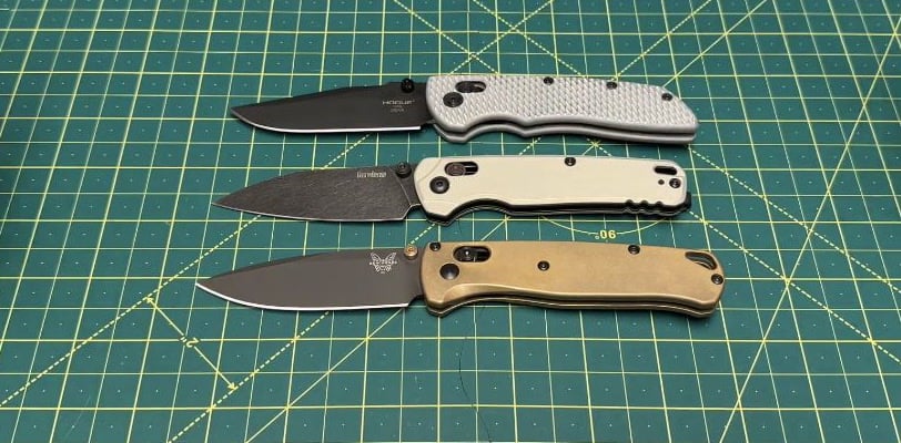Three open knives on a cutting mat, from top to bottom: Hogue Deka with aftermarket scales, Kershaw Bel Air and Benchmade Bugout.